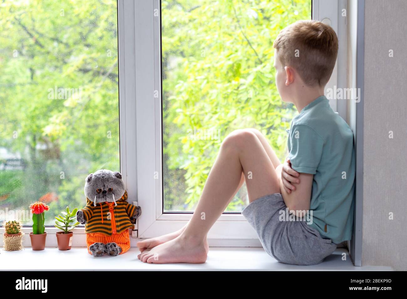 Allein Traurigkeit kaukasischen Jungen auf Fensterbank sitzen, Blick nach draußen während der Pandemie von Coronavirus Covid-19. Fühlt sich unglücklich und einsam. Bleiben Sie zu Hause Stockfoto