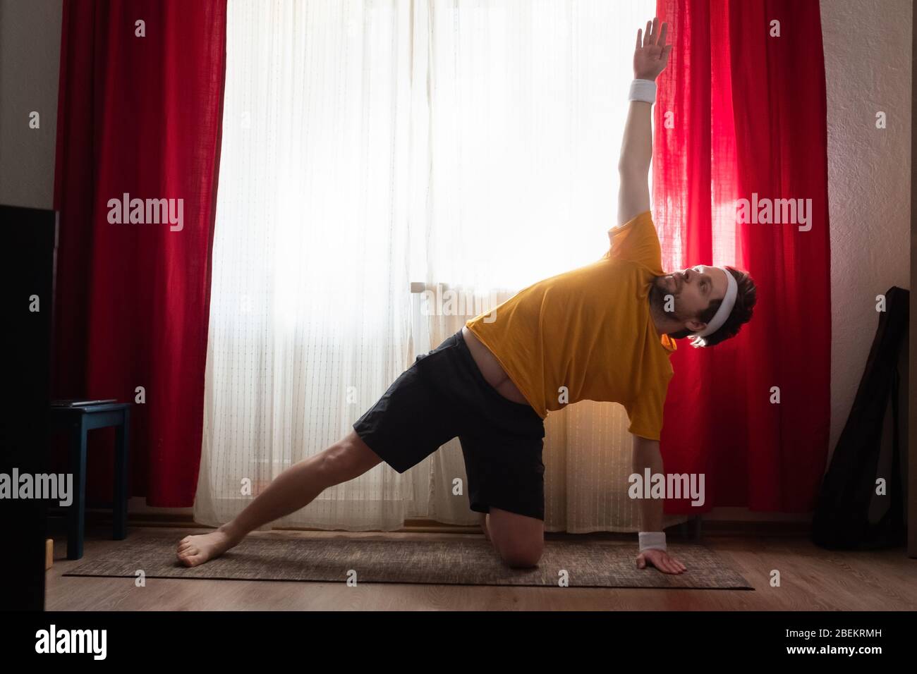 Fröhlicher Mann, der eine seitliche Plank-Übung im Zimmer macht Stockfoto