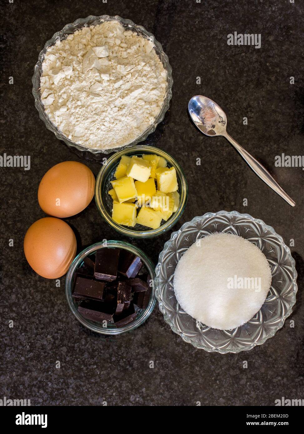 Zutaten für eine Torte, darunter Mehl, Butter, Eier, Schokolade und Zucker auf dunklem Hintergrund Stockfoto