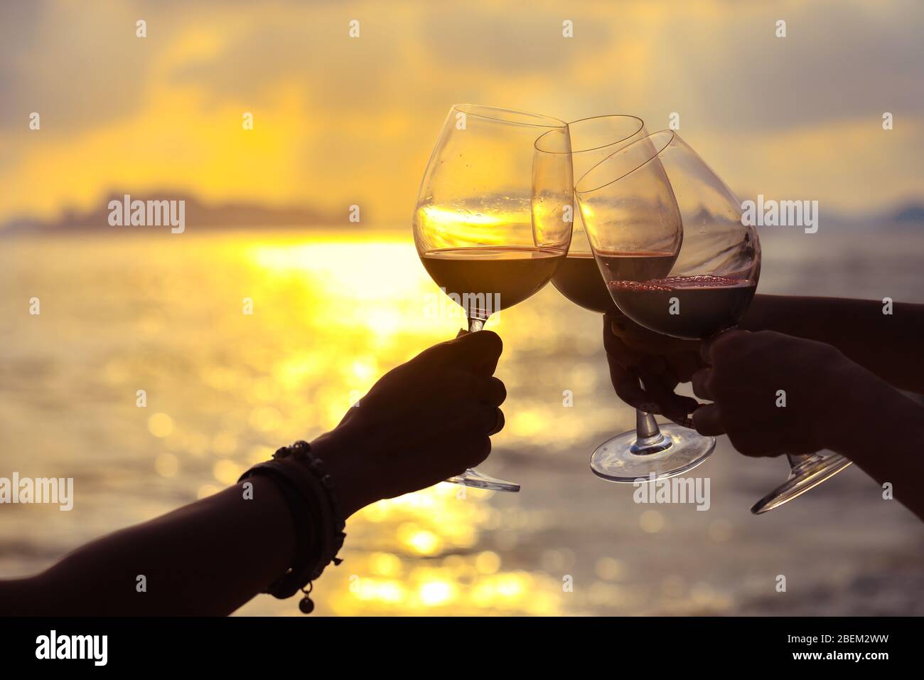 Nahaufnahme der Hände mit Rotweinglas auf dem Balkon bei Sonnenuntergang, Konzept der Feier Stockfoto
