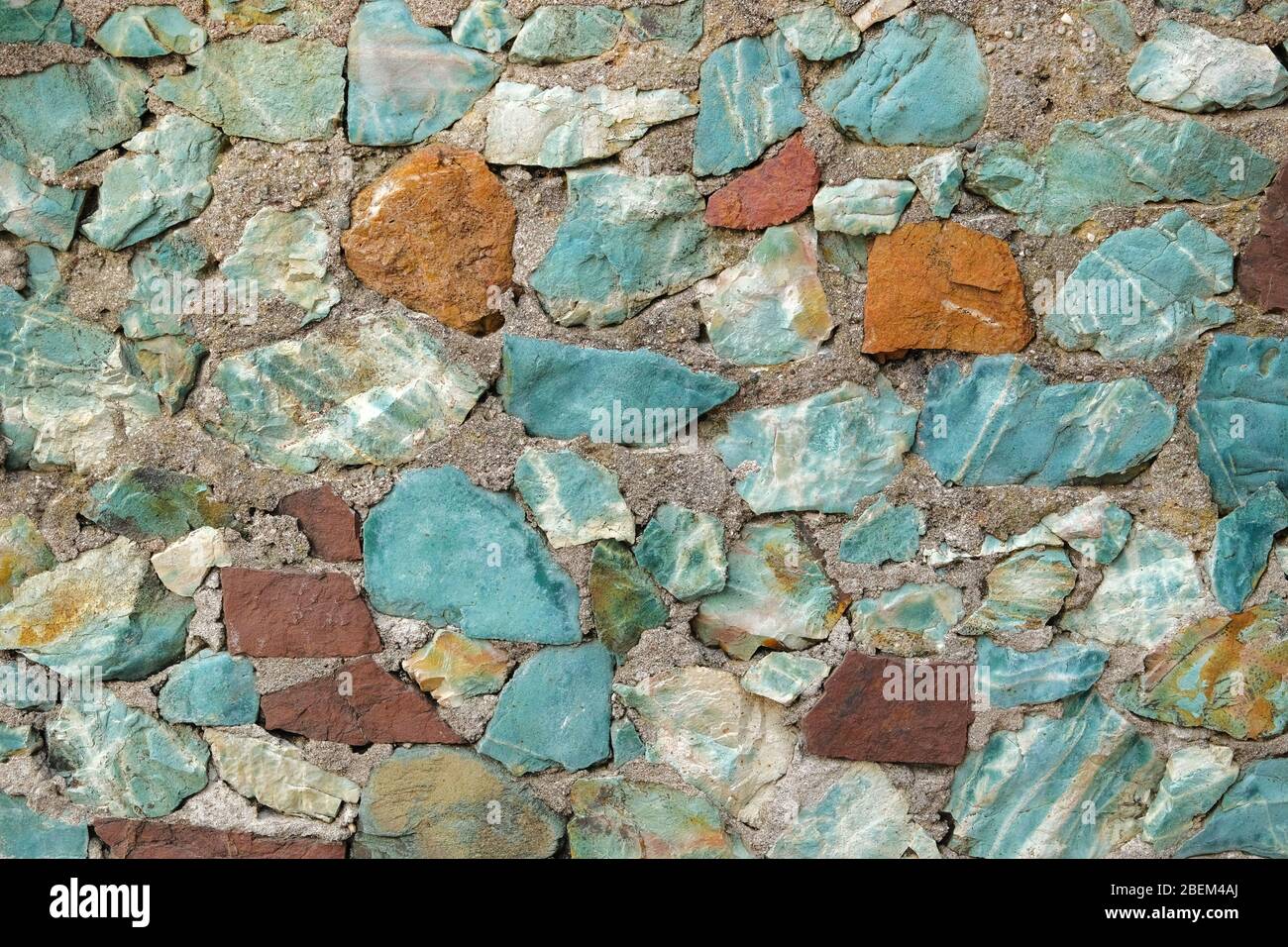 Hintergrund mit türkisfarbenen und braunen Steinen. Wand aus blauen und burgunderroten groben Steinen. Stockfoto