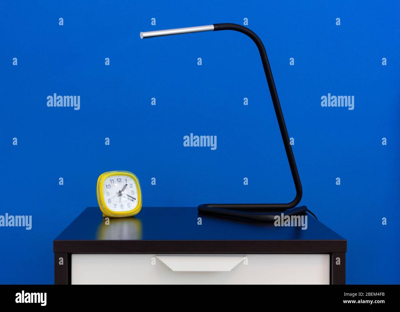 Eine moderne Lampe und ein Wecker auf einem Nachttisch gegen eine blaue Innenwand Stockfoto