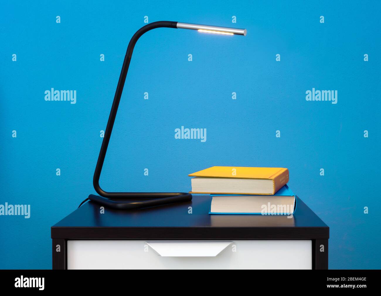 Eine moderne Lampe und zwei Bücher auf einem Nachttisch gegen eine blaue Innenwand Stockfoto