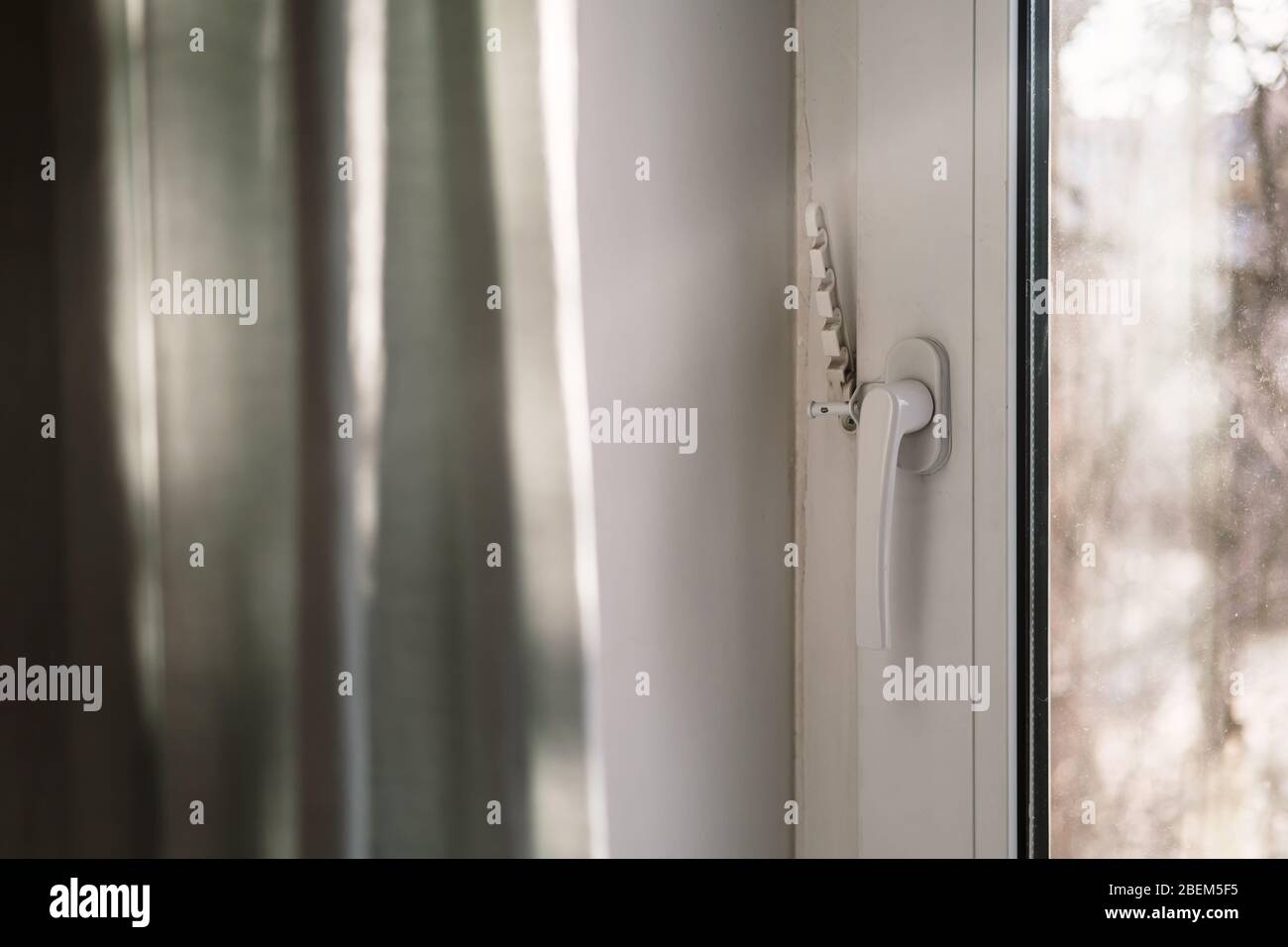 Geschlossenes weißes PVC-Fenster, mit befestigtem Befestigungselement für Belüftung und einem Vorhang in der Sonne, unter natürlichem Licht. Stockfoto