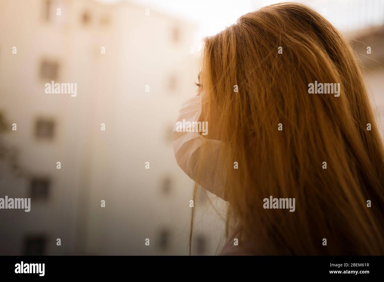 Porträt einer jungen Frau zu Hause Isolation auf einem Balkon stehend, trägt chirurgische Maske. Protokolle zum Schutz vor Coronavirus und zur Prävention. Bleiben Sie zu Hause. Stockfoto