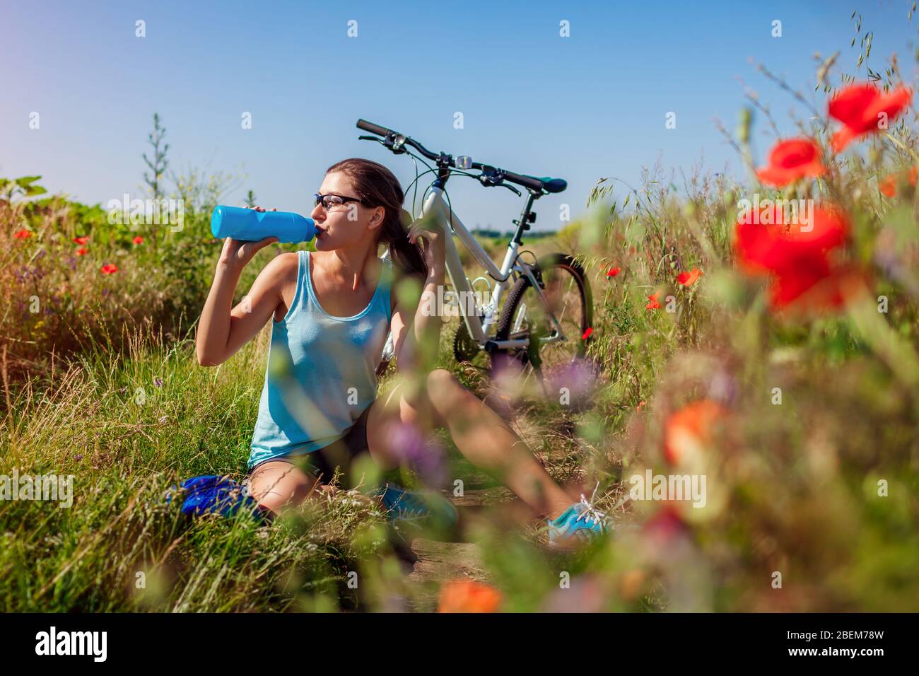 Glückliche junge Frau Radfahrer Trinkwasser und mit Ruhe nach Fahrrad in Sommerfeld unter Blumen fahren. Sport Stockfoto
