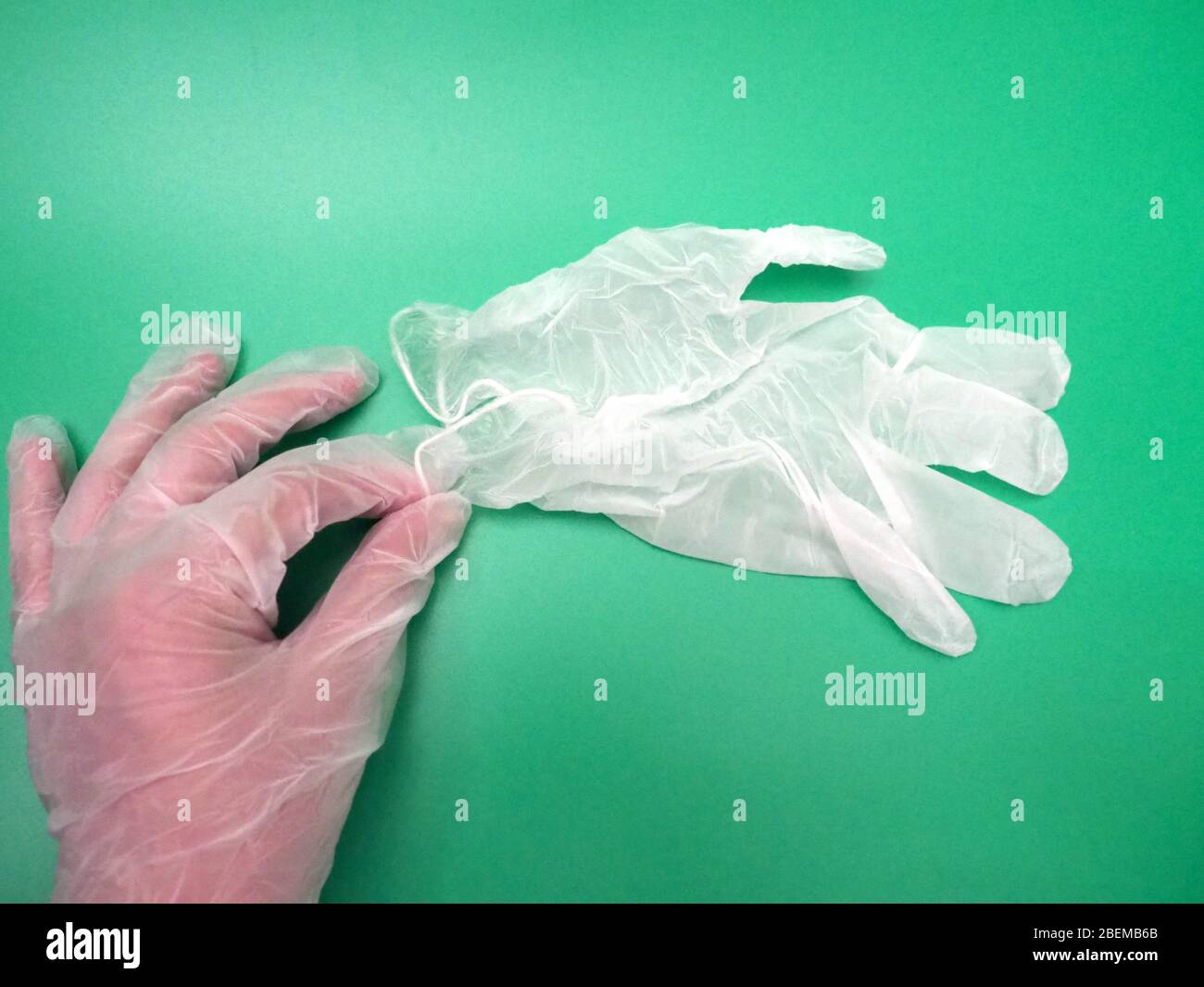 Hand mit EINEM weißen Einweghandschuh (PSA), der nach draußen greift und einen weiteren weißen Einweghandschuh in London, Großbritannien, in die Hand nimmt Stockfoto