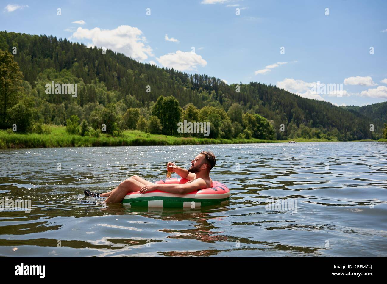 Das Leben genießen. Junger Mann, der sich mit einem Glas Bier auf dem Fluss ausruht. Entspannung, Urlaub, Lifestyle-Konzept Stockfoto