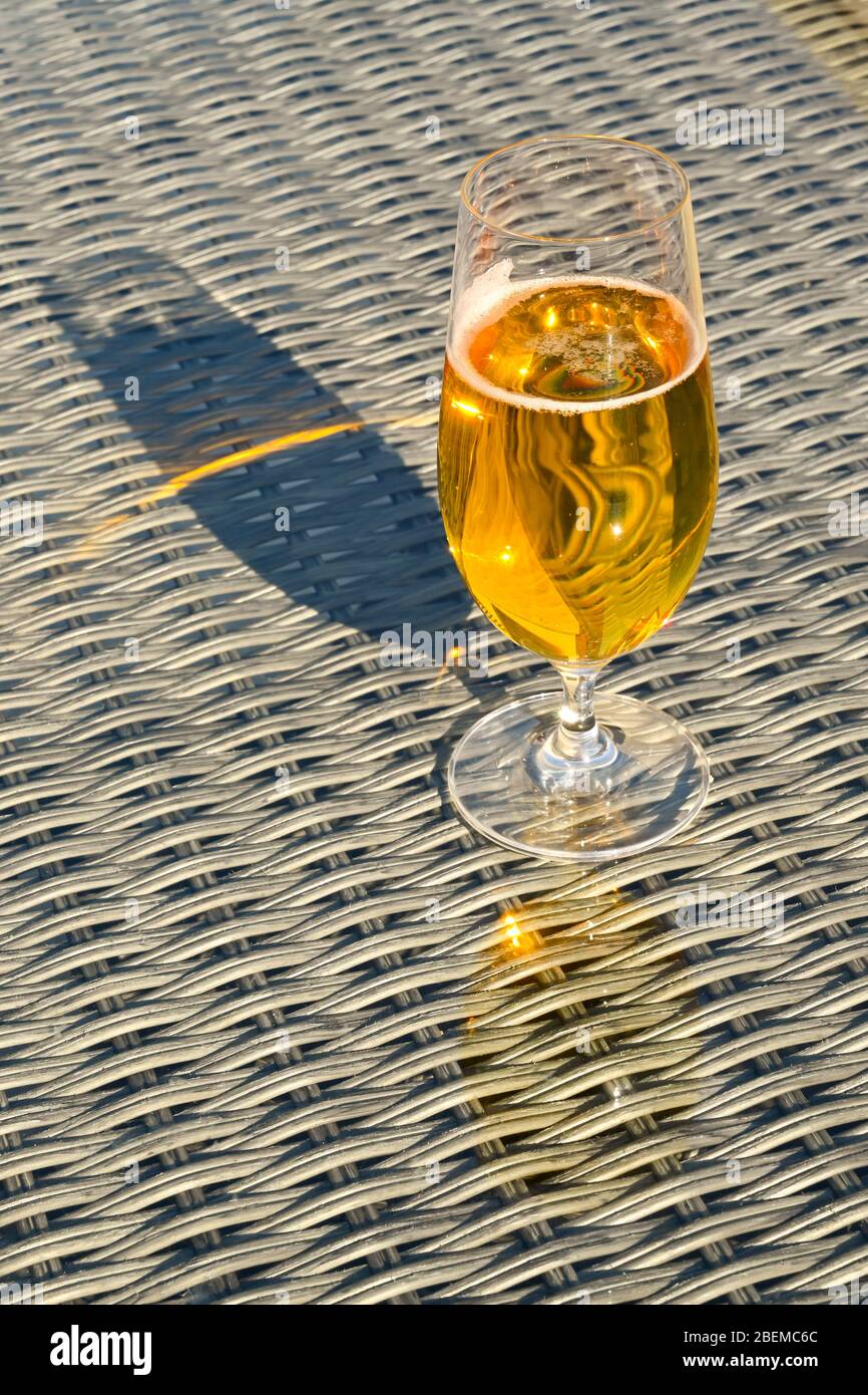 Glas goldenes Bierlager auf der Glastisch-Tischplatte der Gartenmöbel Stockfoto