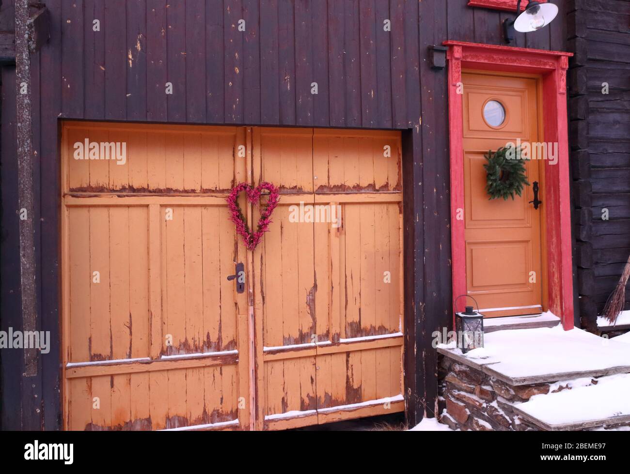 Nahaufnahme einer orangefarbenen Tür und eines Tores mit charmanten Details eines traditionellen Holzhauses in der historischen Bergbaustadt Røros im Winter Stockfoto