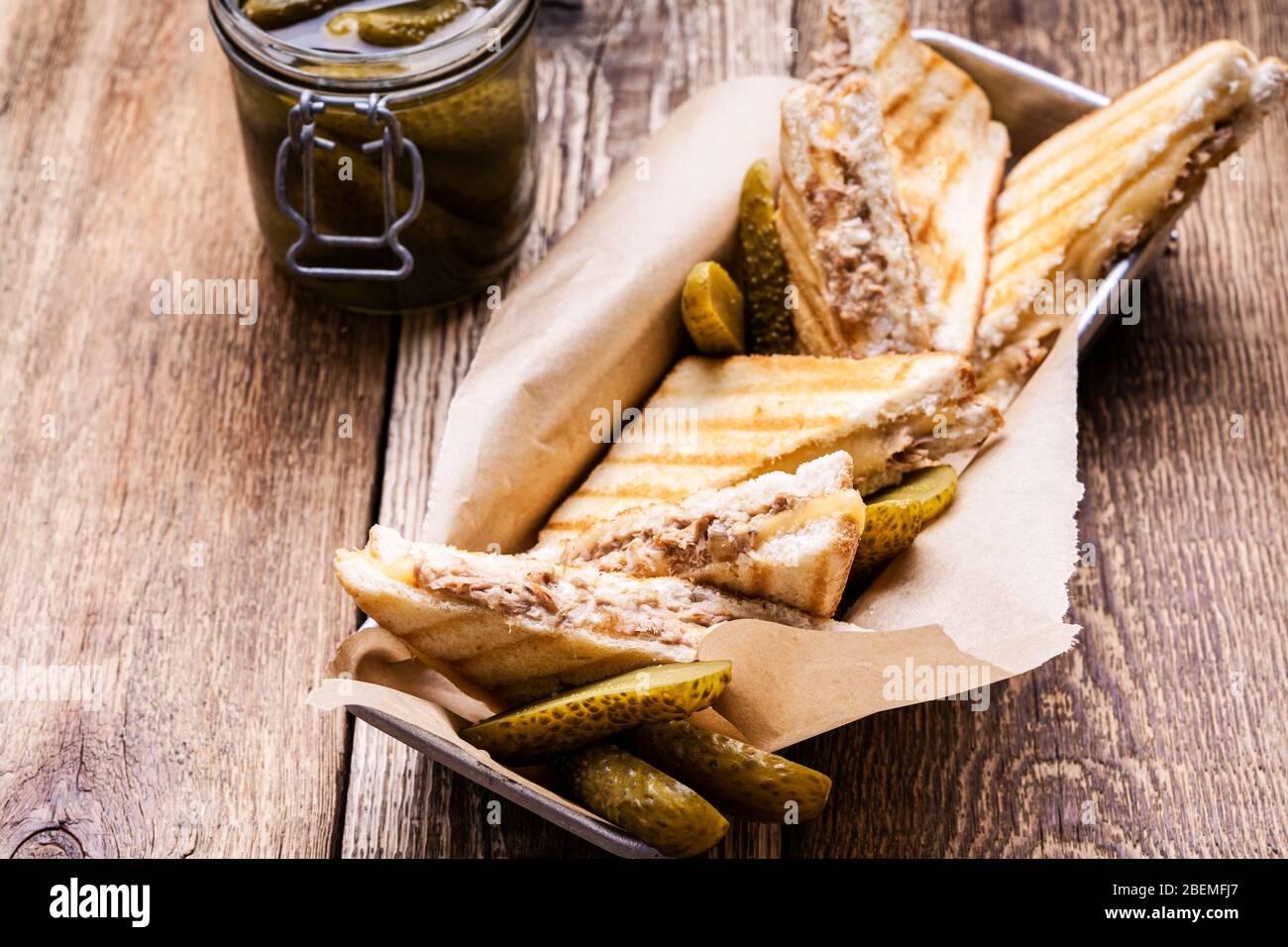 Hausgemachte Thunfisch-Sandwiches mit Käse serviert mit Gurken auf rustikalem Holztisch Stockfoto