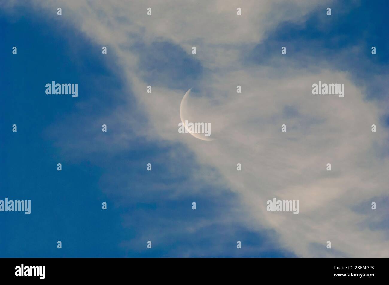 Ein schmaler silberner Mondschein, der auf einer Fläche eines teilweise bewölkten blauen Himmels aufgeht. Stockfoto