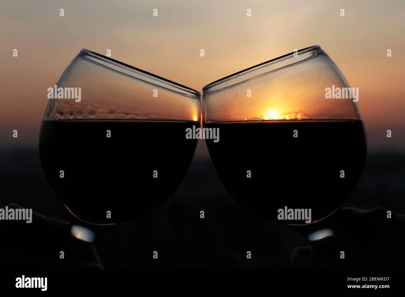 Zwei Gläser mit Rotwein auf buntem Sonnenuntergang Hintergrund. Paar klirren Gläser, Konzept der Feier, romantischen Abend zu Hause Quarantäne, Liebe Datum Stockfoto