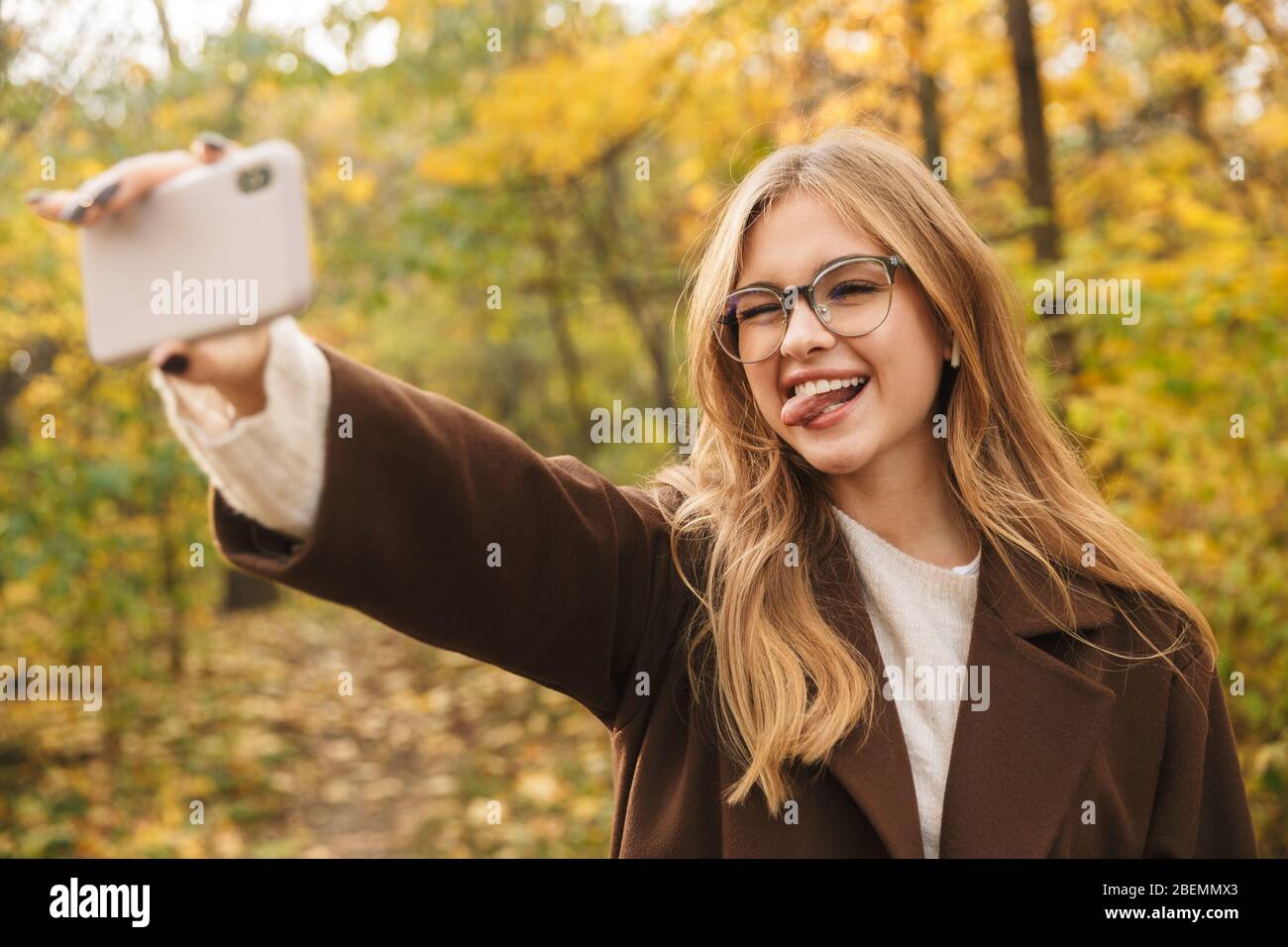 Schöne junge fröhliche Frau trägt Mantel Wandern im Herbst Park, ein Selfie zu machen Stockfoto