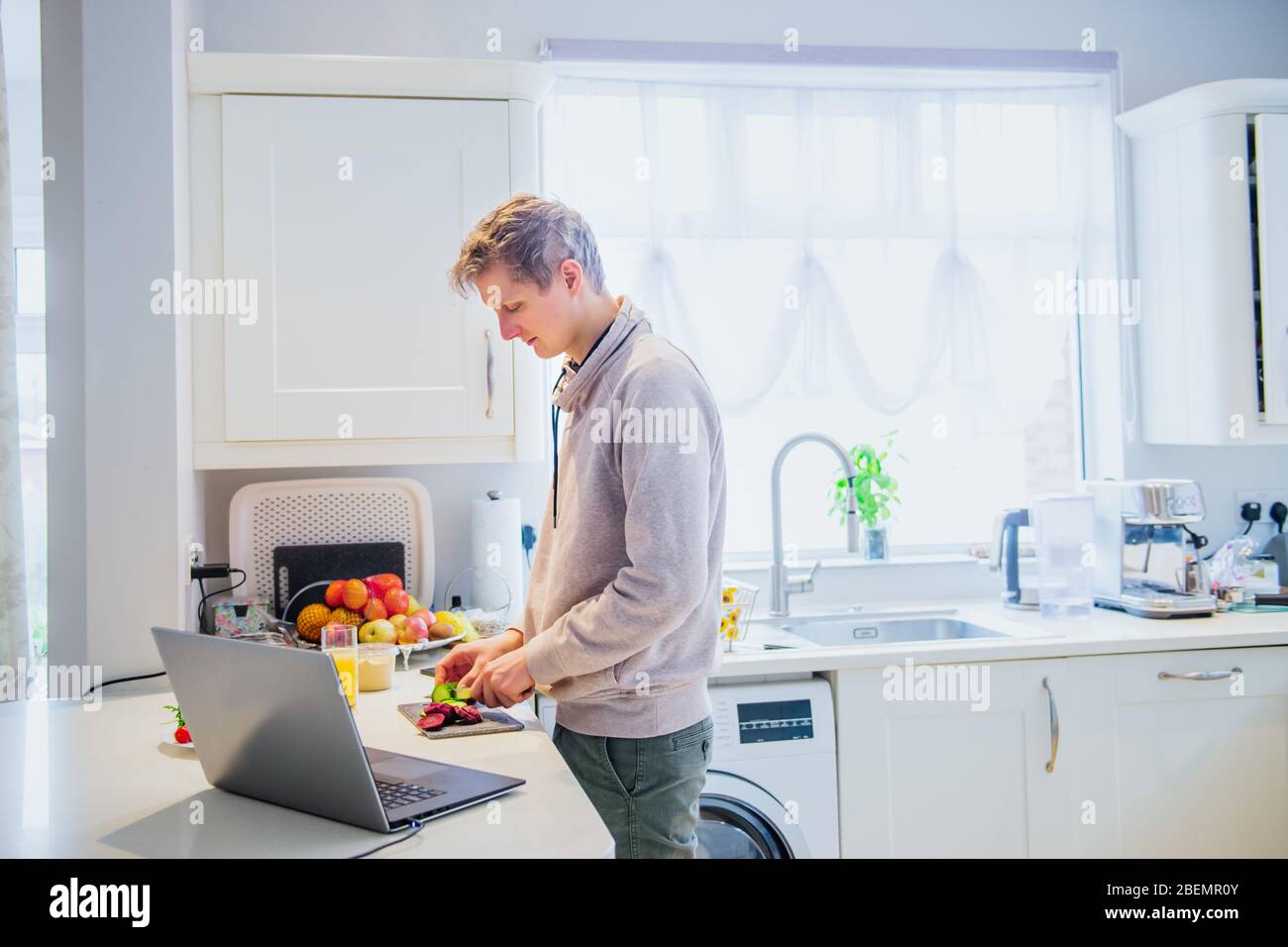 Junger kaukasischer Mann, der von zu Hause aus arbeitet. Freiberufliche Küche vegetarisches Mittagessen am Küchentisch und Arbeit am pc-Laptop. Heimbüro, ferne Arbeitsplatte Stockfoto