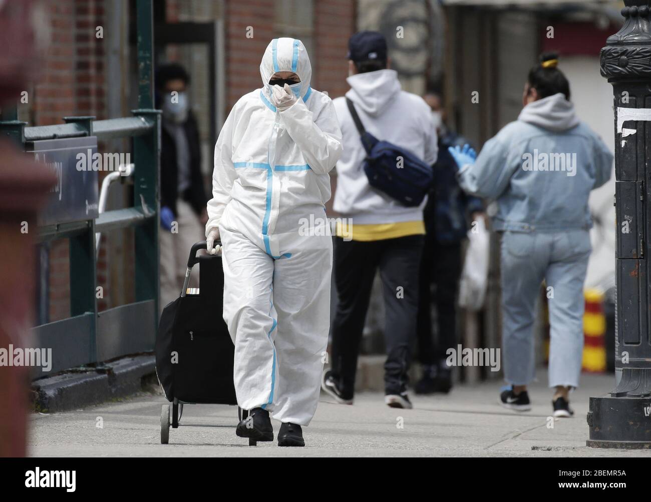 Brooklyn, Usa. April 2020. Ein Fußgänger, der Kopf bis Fuß in Schutzkleidung überdeckt, kreuzt am Dienstag, den 14. April 2020, auf dem Bürgersteig in der Nähe des Wyckoff Heights Medical Center in New York City. Bis heute sind fast 285,000 Menschen mit dem Coronavirus infiziert und mehr als 14,000 Menschen sind in NY, NJ und CT gestorben. Es gibt jedoch Anzeichen dafür, dass die Kurve abflacht. Foto von John Angelillo/UPI Quelle: UPI/Alamy Live News Stockfoto