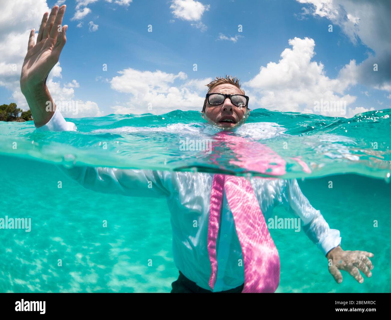 Über-unter Ansicht des Geschäftsmannes, der seine Hand oben hält, um Hilfe zu rufen versucht, in klarem türkisfarbenem Wasser über Wasser zu halten Stockfoto