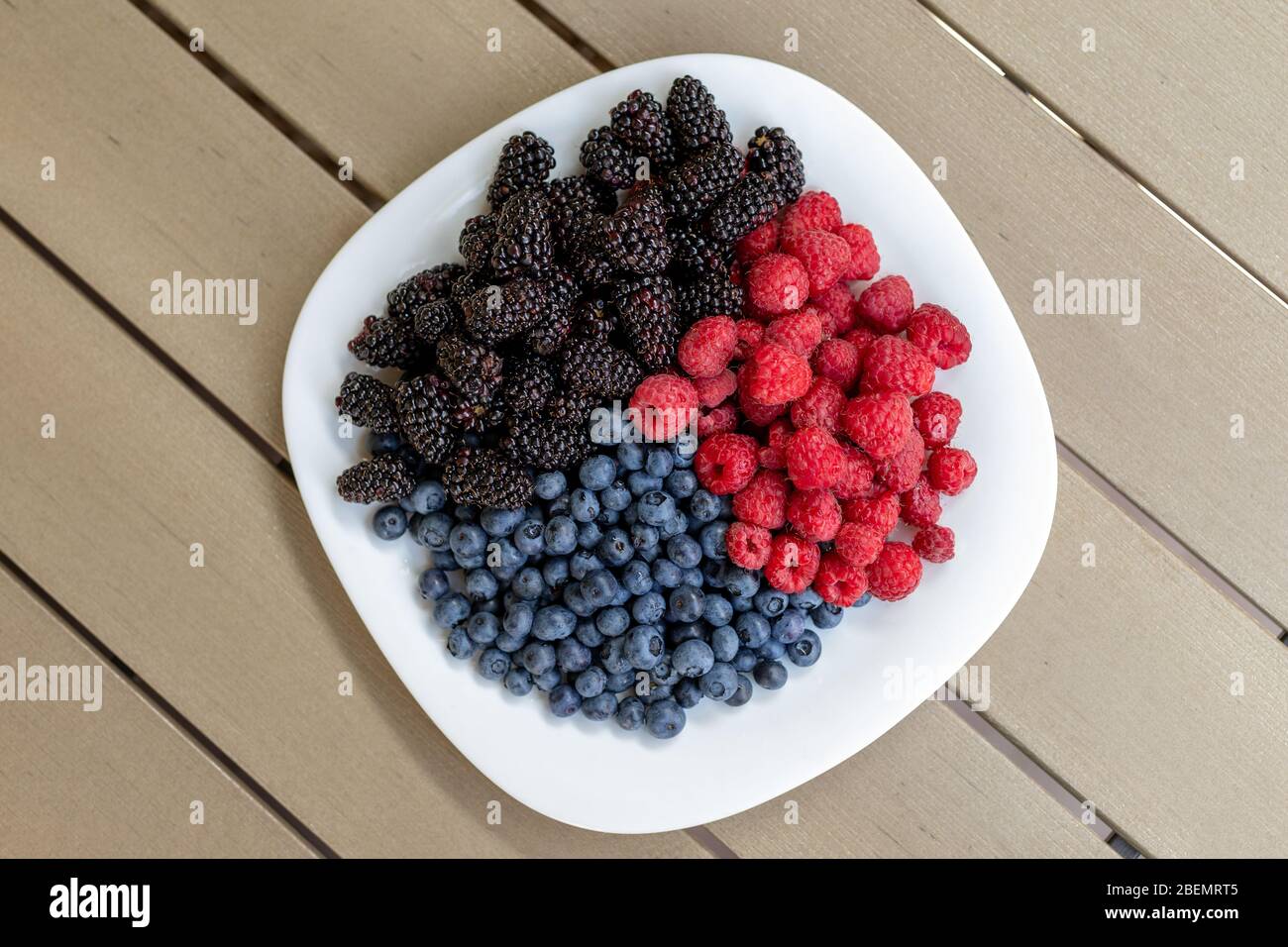 Weißer Keramikplatte mit saftigen Bio-Beeren der Saison als Snack. Reife leckere frische Himbeere, Brombeere und Heidelbeere Sommer Mischung für Stockfoto