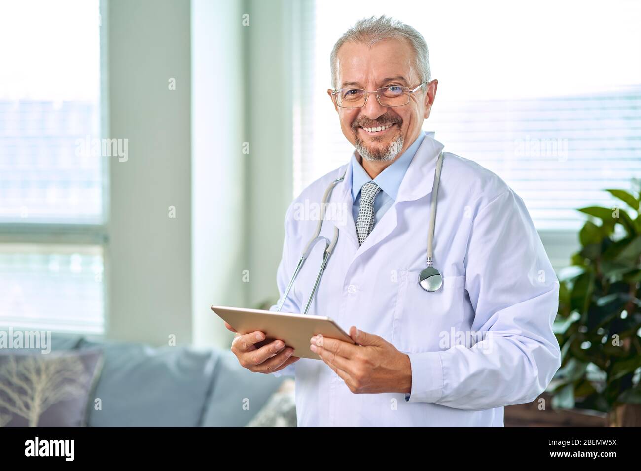 Medizinische leitender Arzt mit einem Stethoskop. Auf einem blauen Hintergrund. Ein medic hält eine Tablette in der Hand und macht einen Termin mit der Klinik. Krankheit Stockfoto