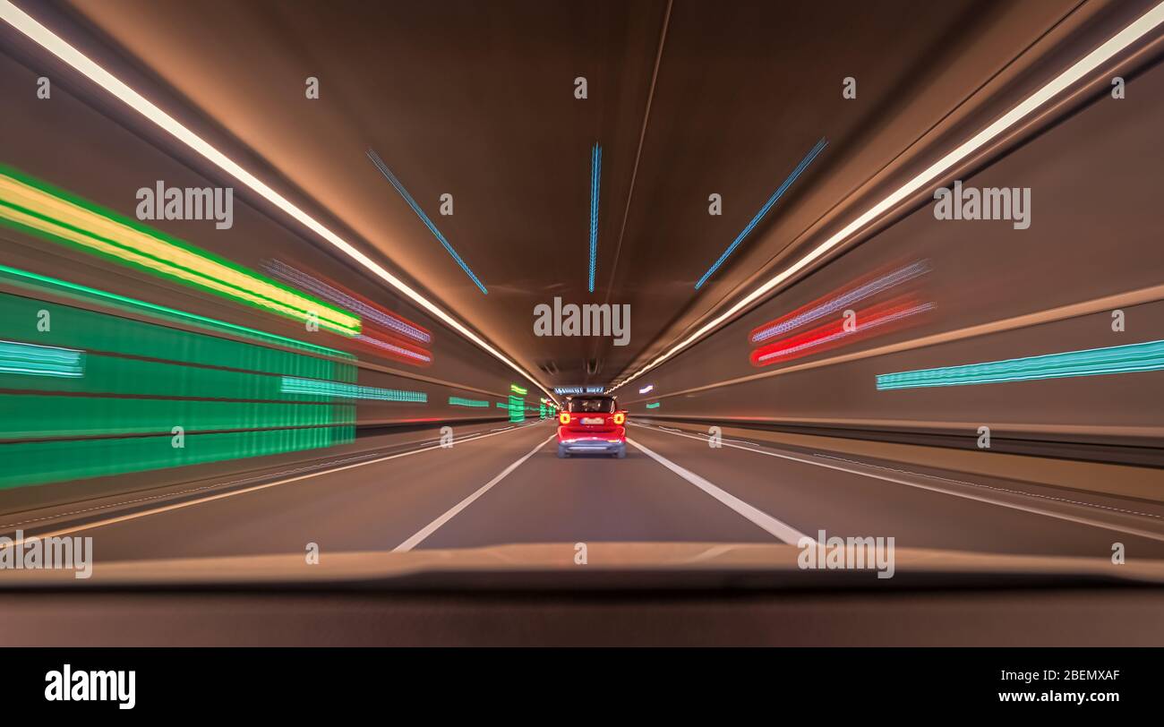 Schnell fahrende Autos durch einen Tunnel mit unscharfen Lichteffekten, eine städtische Rennszene mit führenden Linien und Symmetriestruktur. Stockfoto