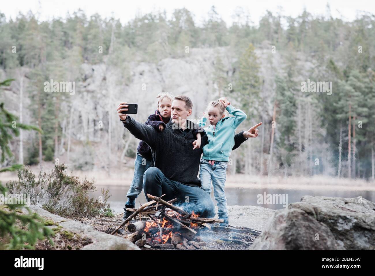 Vater nimmt Selfies mit seinen Kindern, während er neben einem Lagerfeuer sitzt Stockfoto