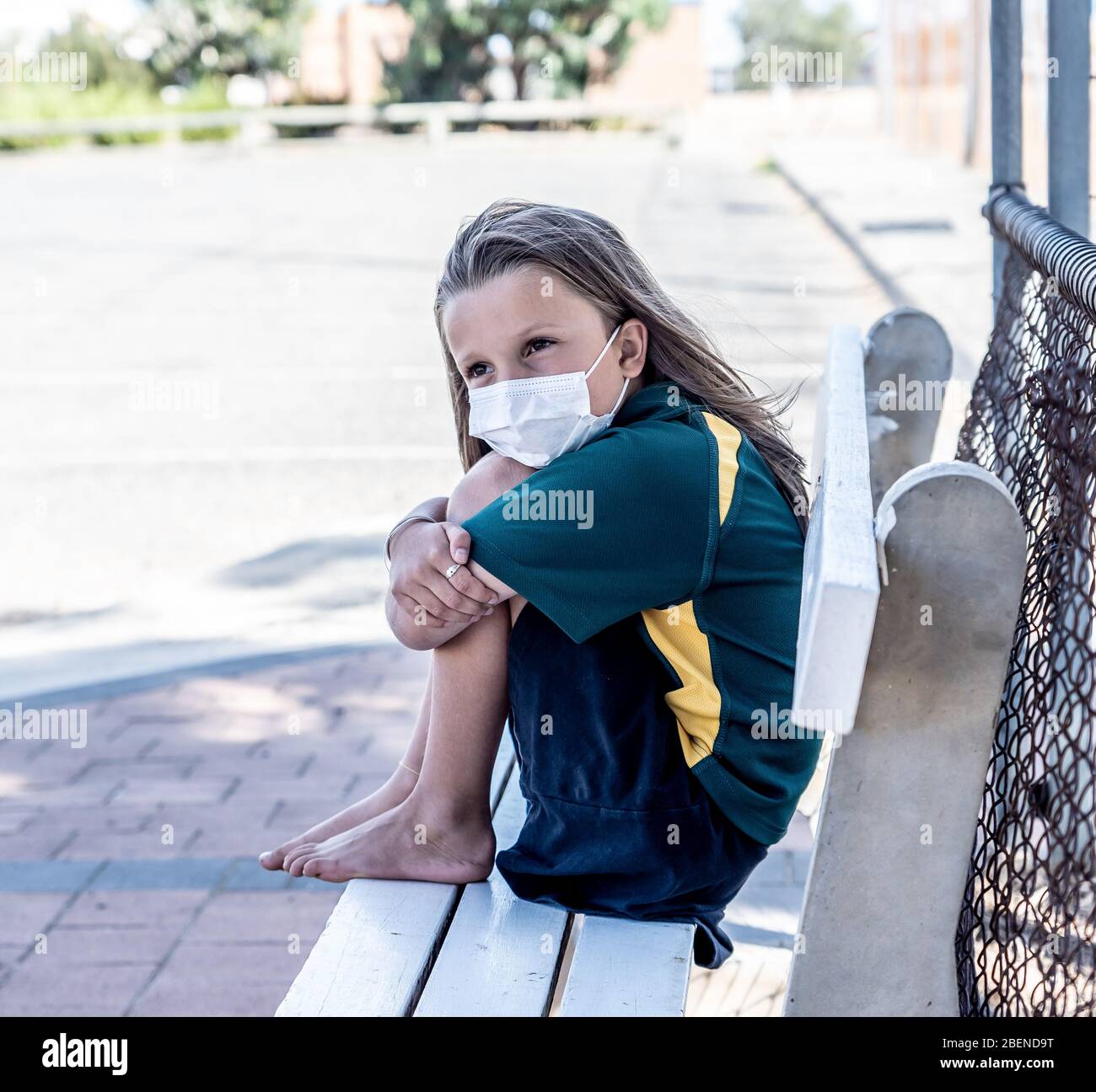 Covid-19 Ausbruchschulen geschlossen. Trauriges und gelangweiltes Schulmädchen Kind mit Gesichtsmaske, das sich depressiv und einsam vor ihrer geschlossenen Schule fühlt. Einschränkungen a Stockfoto