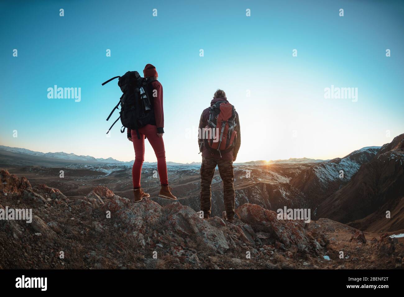 Ein paar junge Wanderer mit großen Rucksäcken stehen und schauen auf Berge und Sonnenuntergang Stockfoto