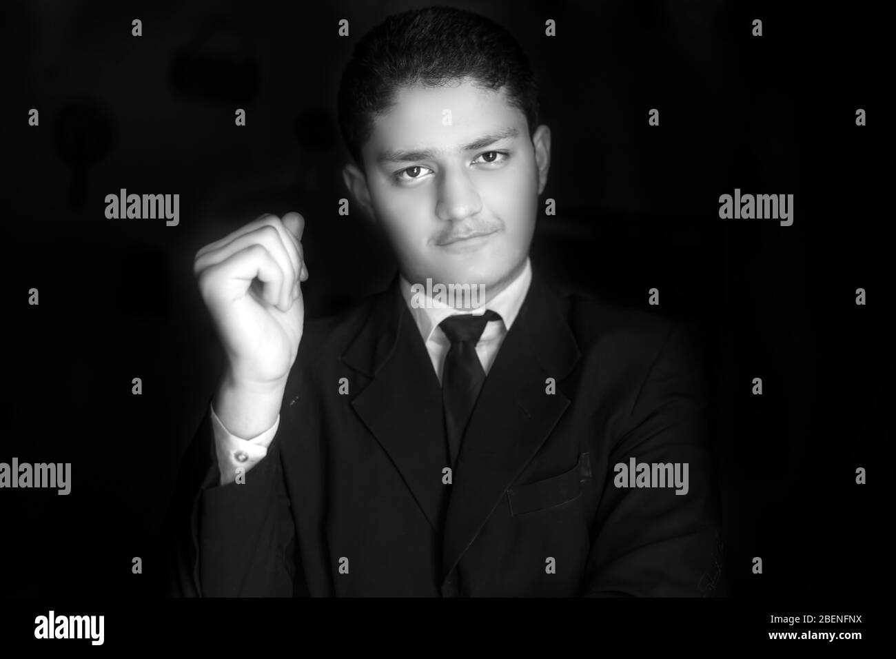 Porträtaufnahme eines jungen Geschäftsmannes, der auf schwarzem Hintergrund mit gekreuzten Händen und rechter Hand in der Nähe seiner Wange posiert. Horizontale Aufnahme von Geschäftsmann in blu Stockfoto
