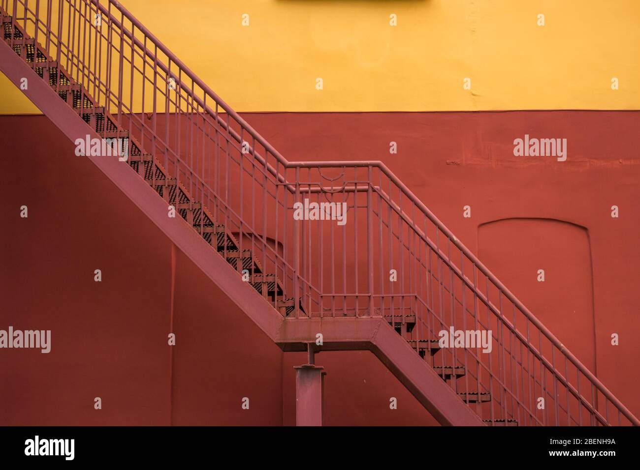 Modernes Gebäude ist burgundergelb mit einer Feuertreppe am Notausgang an der Fassade. Konzeptioneller Hintergrund. Stockfoto