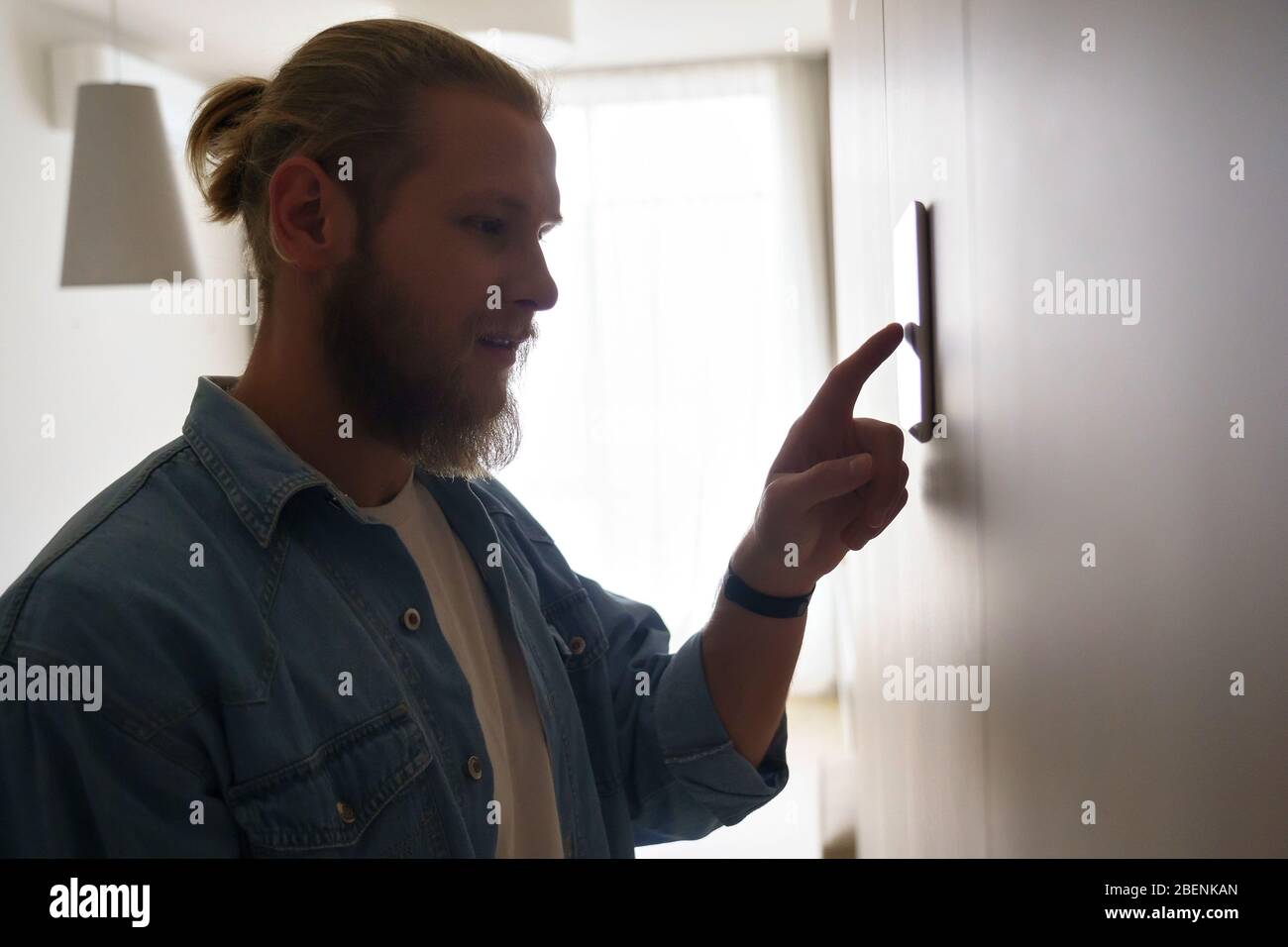 Junger Mann mit Smart Home Thermostat-Technologie-Gerät an der Wand. Stockfoto