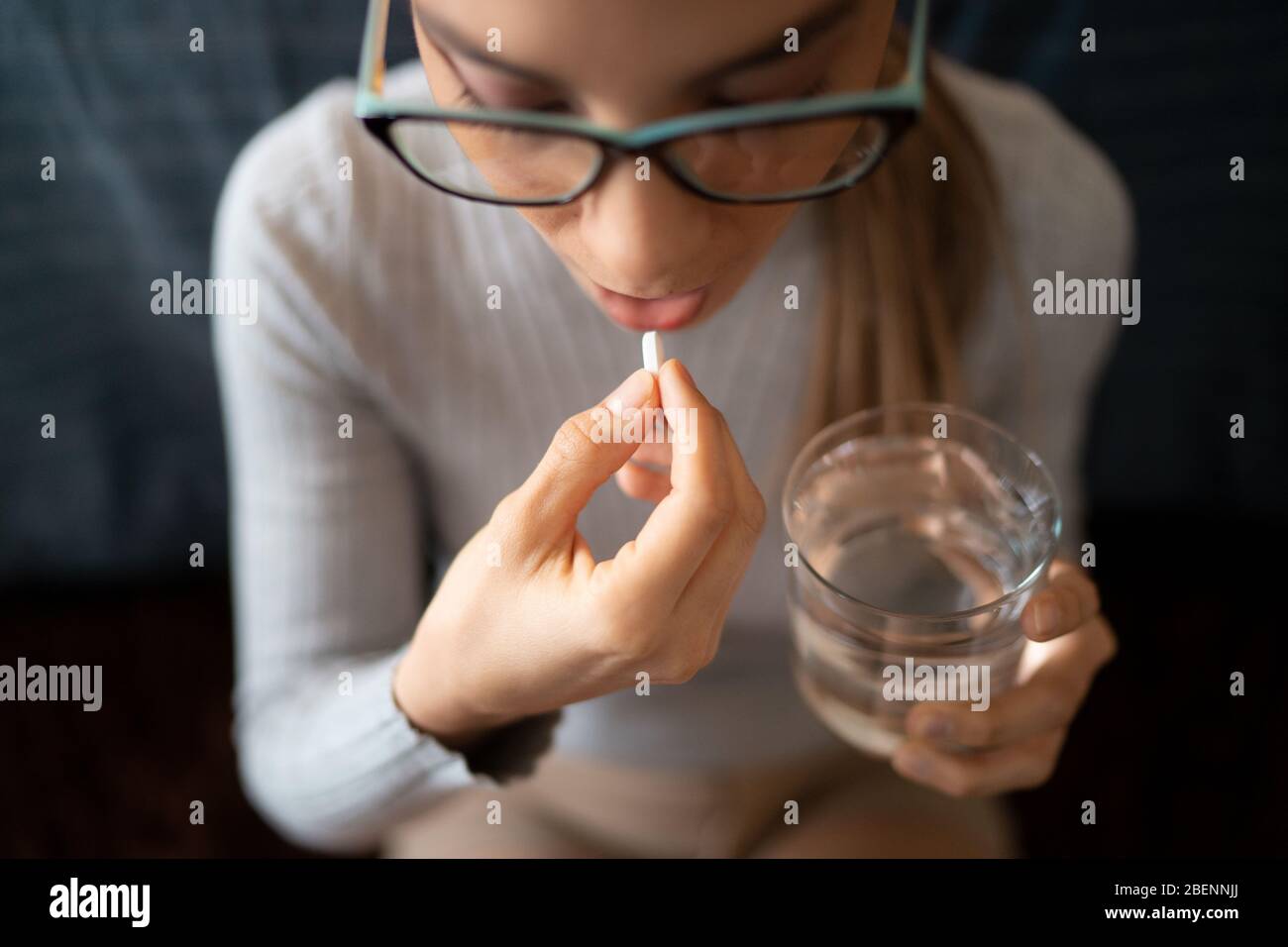Eine junge kranke weiße Frau zu Hause schluckt ihre medizinischen Behandlung Pillen mit einem Glas Wasser. Stockfoto
