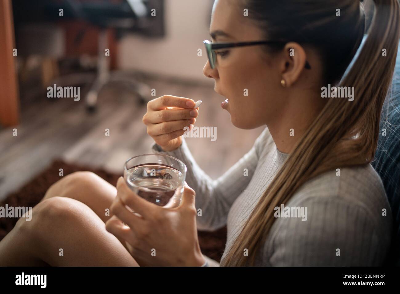 Seitenansicht EINER jungen kranken weißen Frau zu Hause schlucken ihre medizinische Behandlung Pillen mit einem Glas Wasser. Stockfoto