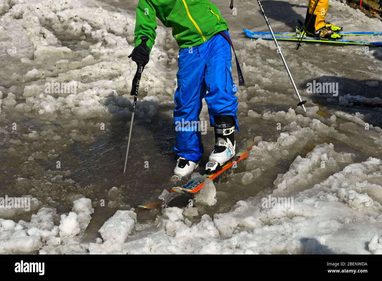 Skifahrer waten mit Skiern durch Slush und Pfütze am Ende der Skisaison, Chamonix, Haute-Savoie, Frankreich Stockfoto