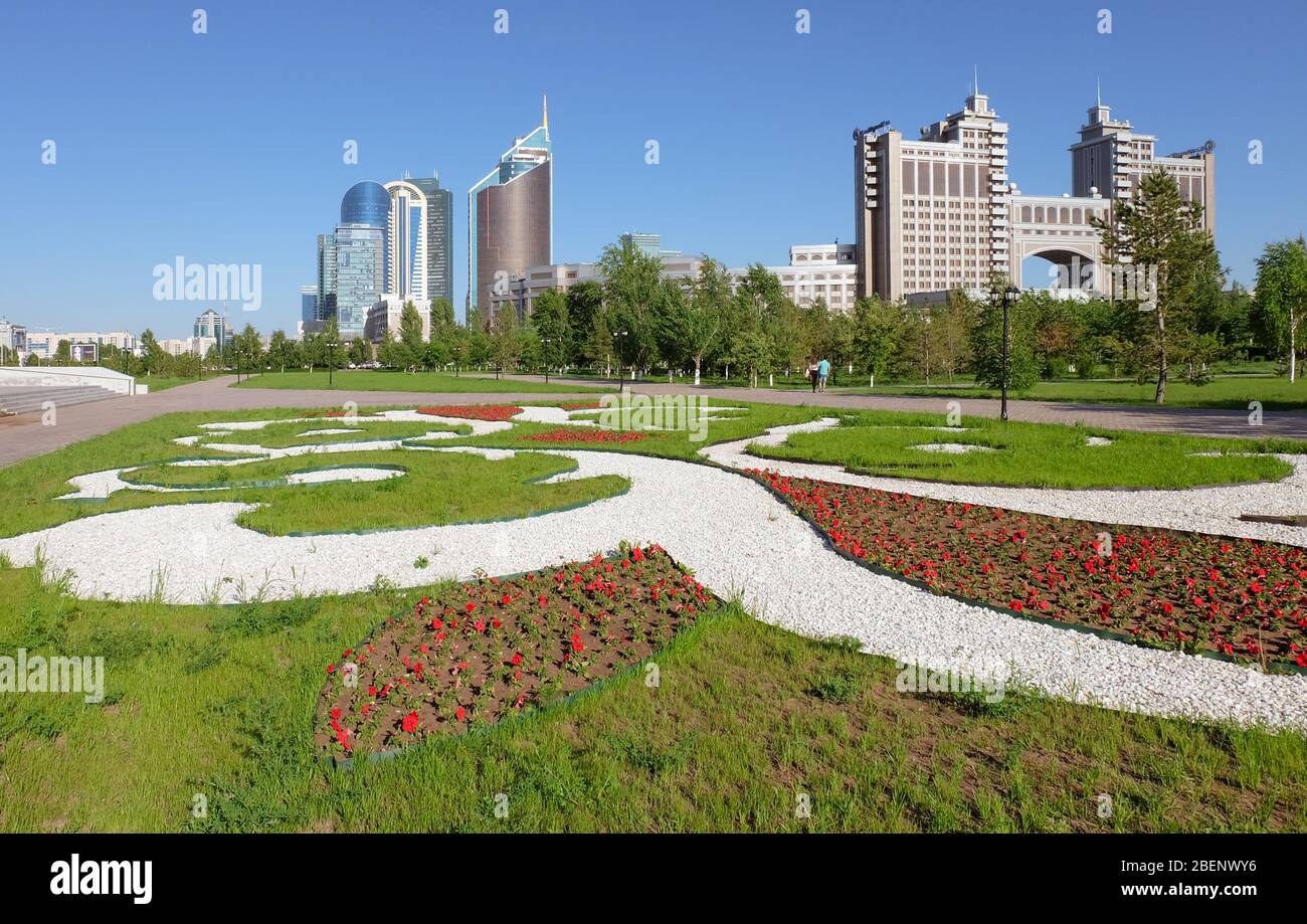 NUR-SULTAN, ASTANA, KASACHSTAN - 3. JUNI 2015: Blick auf das Blumenbeet mit Ornamenten von Petunia-Blumen mit Skyscaper-Gebäuden und KazMunayGas Stockfoto