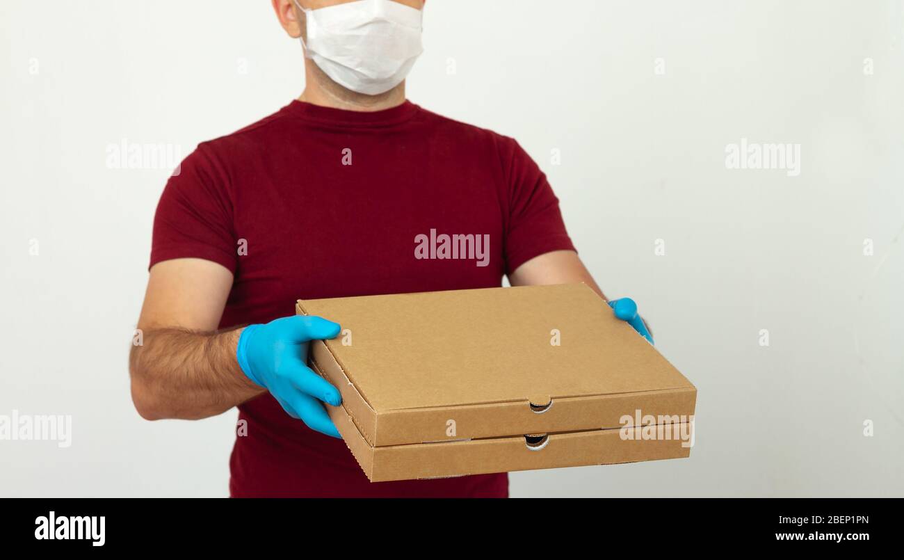 Ein Kurier in medizinischen Handschuhen und Maske hält Pizzakartons. Pizzalieferung während der Quarantäne. Kontaktlose Lieferung Stockfoto