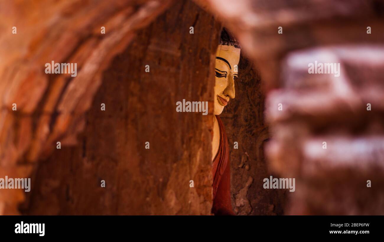 Blick auf eine buddhistische Statue in roten Tönen durch eine Bogentür in Bagan, Myanmar Stockfoto