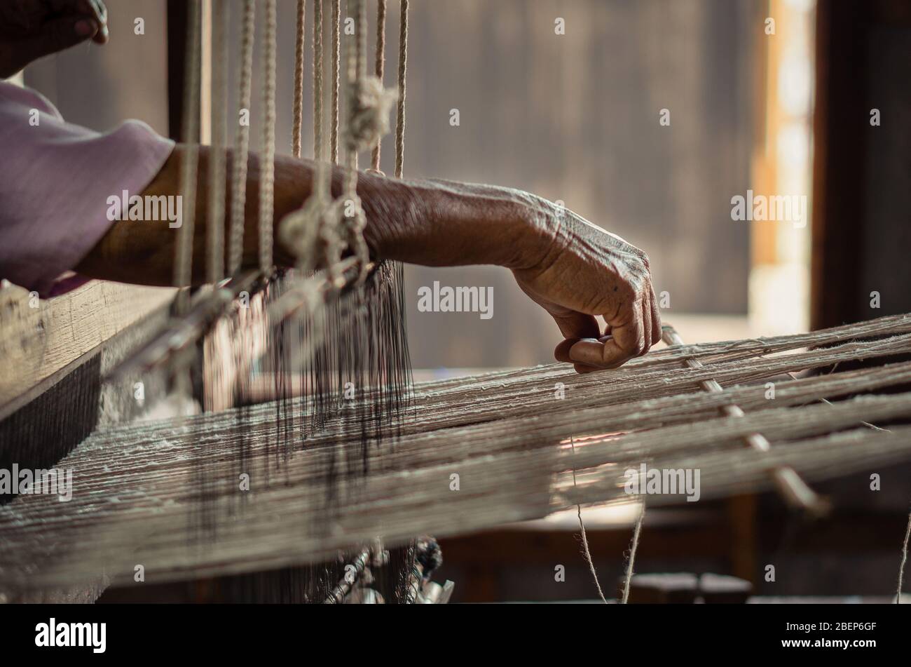 Alte Frau, die mit ihren Händen an einem rustikalen Webstuhl arbeitet Stockfoto