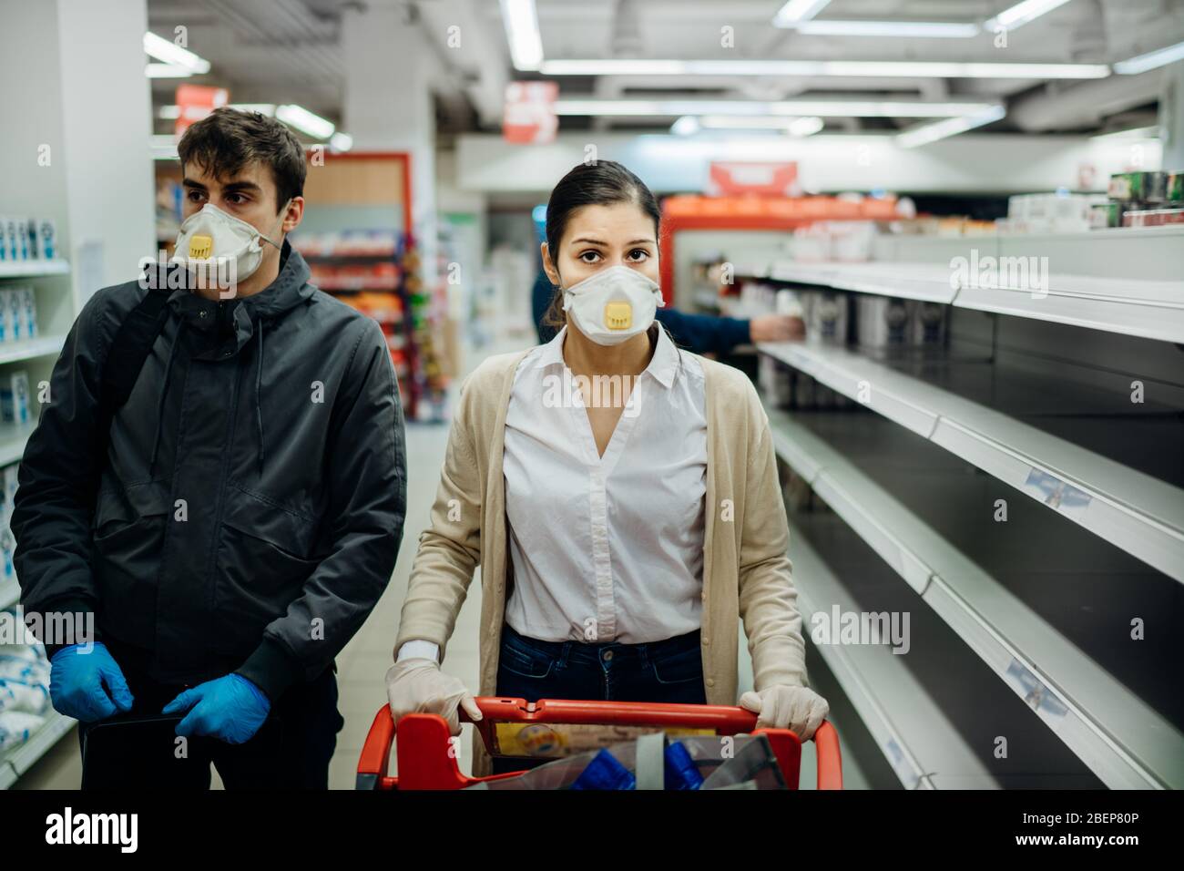 Paar tragen Masken und Handschuhe Kauf Lebensmittel / Vorräte im Supermarkt mit ausverkauften Produkten.Lebensmittel Mangel.leere Regale aufgrund von Corona Stockfoto
