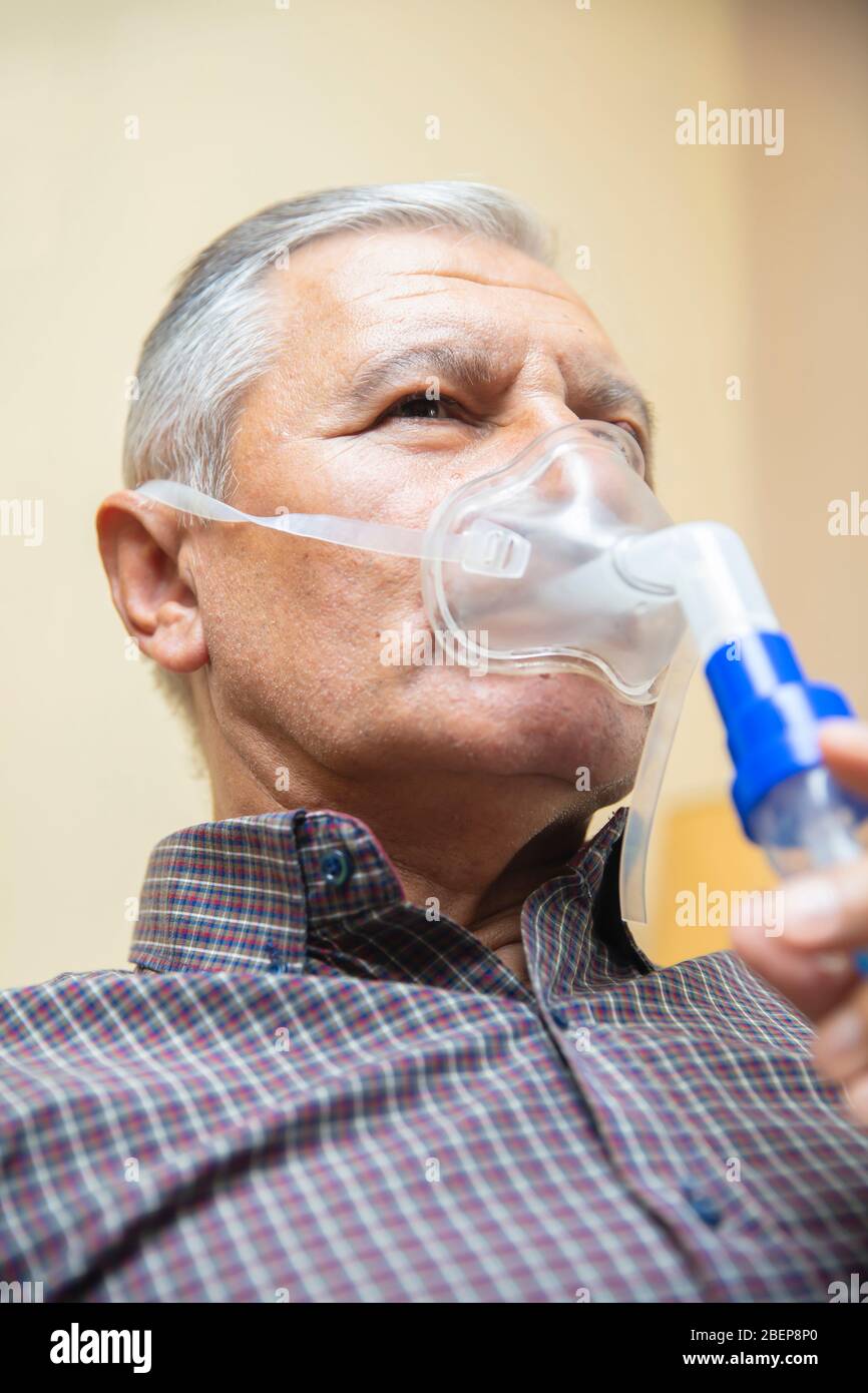 Leitender Mann, der medizinische Geräte für die Inhalation mit Atemschutzmaske verwendet, Vernebler im Zimmer Stockfoto
