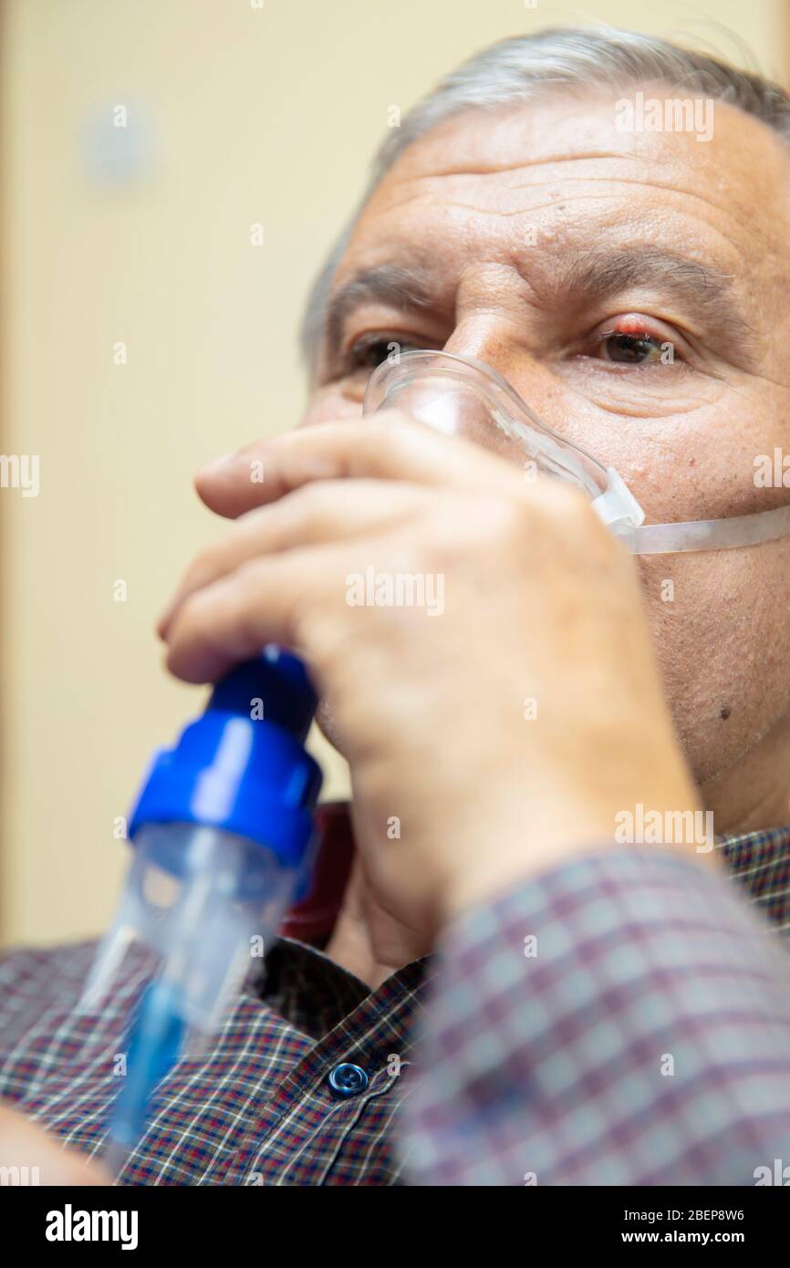 Leitender Mann, der medizinische Geräte für die Inhalation mit Atemschutzmaske verwendet, Vernebler im Zimmer Stockfoto