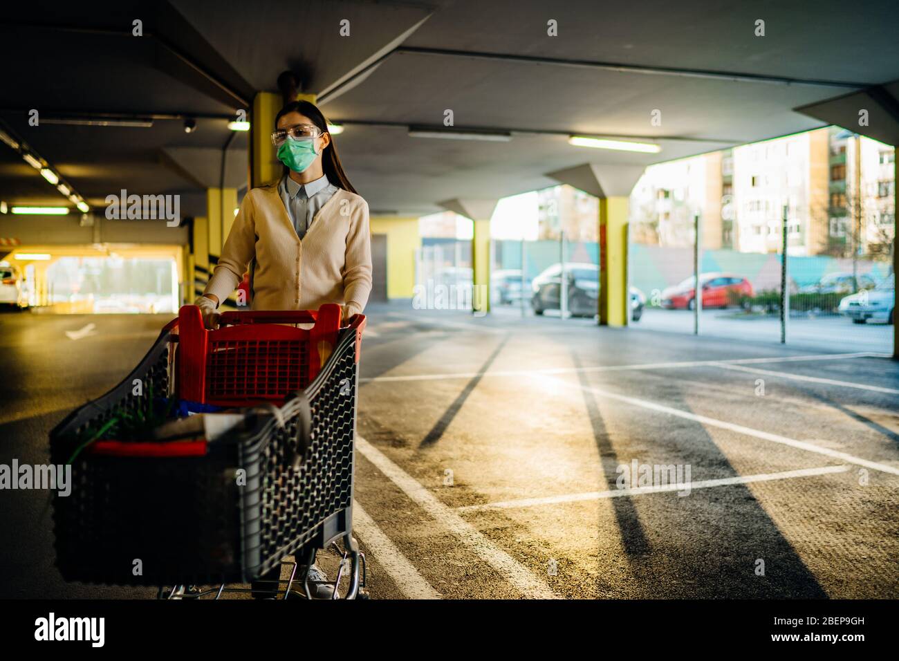 Frau, die Maske Lebensmittel / Lieferungen Einkaufen im Supermarkt, schieben Trolley.Food Lieferungen Mangel.Panik Kauf und horten.Empty Parkhaus.Su Stockfoto
