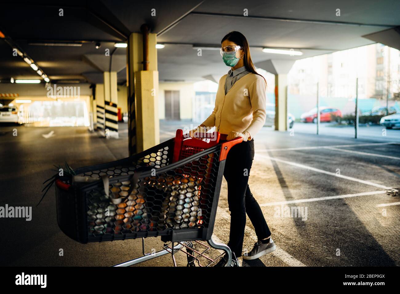 Frau, die Maske Lebensmittel / Lieferungen Einkaufen im Supermarkt, schieben Trolley.Food Lieferungen Mangel.Panik Kauf und horten.Empty Parkhaus.Su Stockfoto