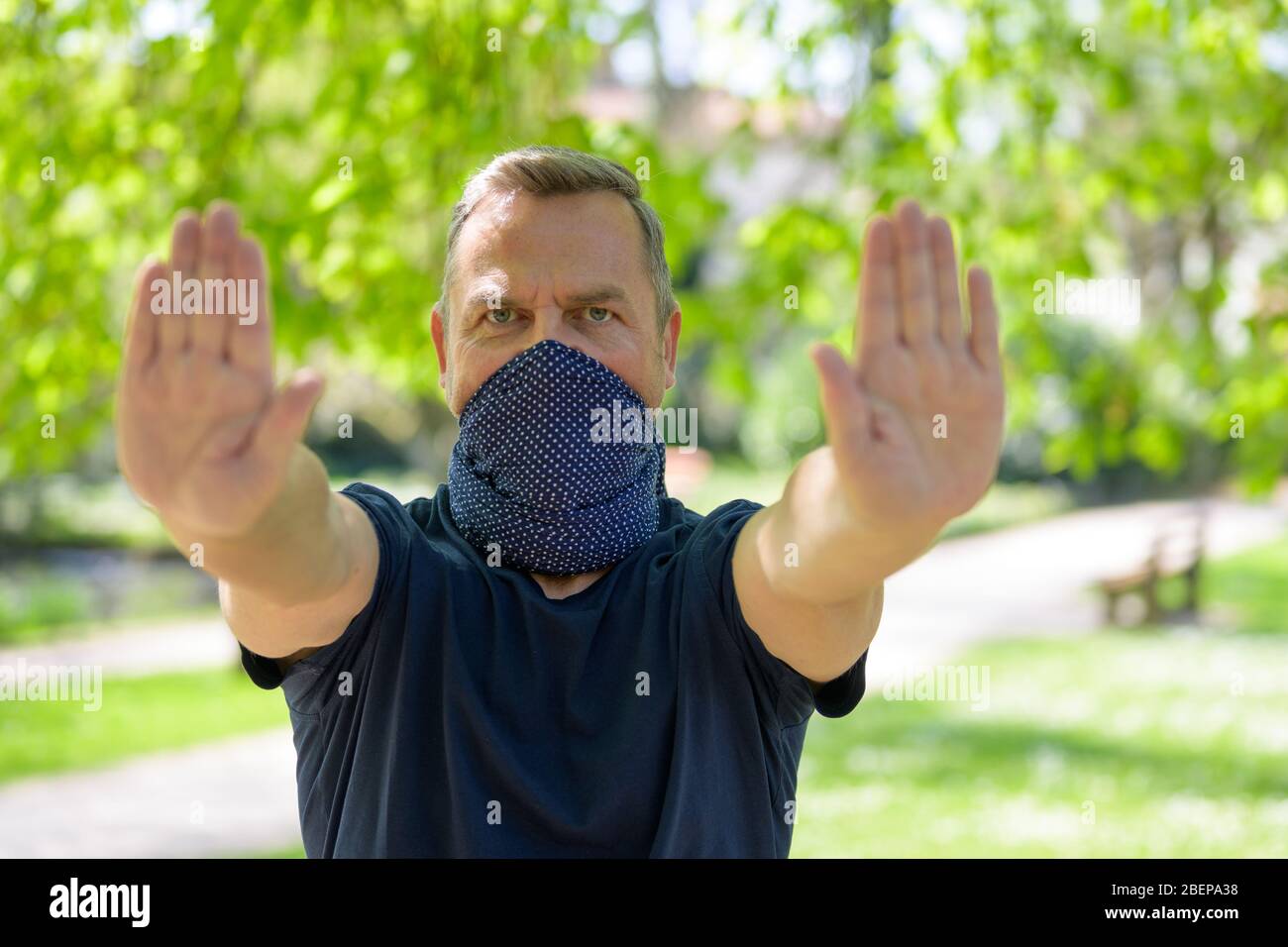 Mann trägt Gesichtsschutz, um eine Infektion zu verhindern, hält seine Hände in einer Geste Halt, um zu verhindern, dass jemand in einem Frühlingspark während der Coronavi nähert Stockfoto