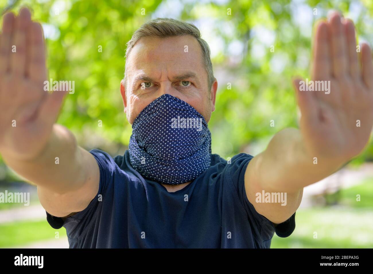 Entschlossener Mann, der einen Gesichtsschutz trägt und mit beiden Händen einen Halt ruft, um zu verhindern, dass sich jemand während des Coronavir im Freien in einem Park nähert Stockfoto