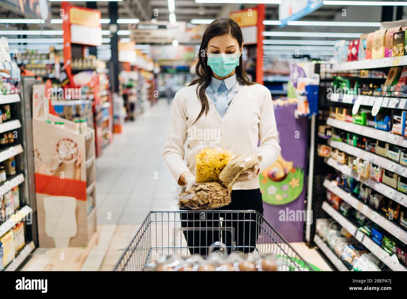 Frau mit Maske sicher einkaufen für Lebensmittel inmitten der Coronavirus-Pandemie in einem sortierten Lebensmittelgeschäft.COVID-19 Lebensmittel im Supermarkt kaufen.Panik kaufen Stockfoto