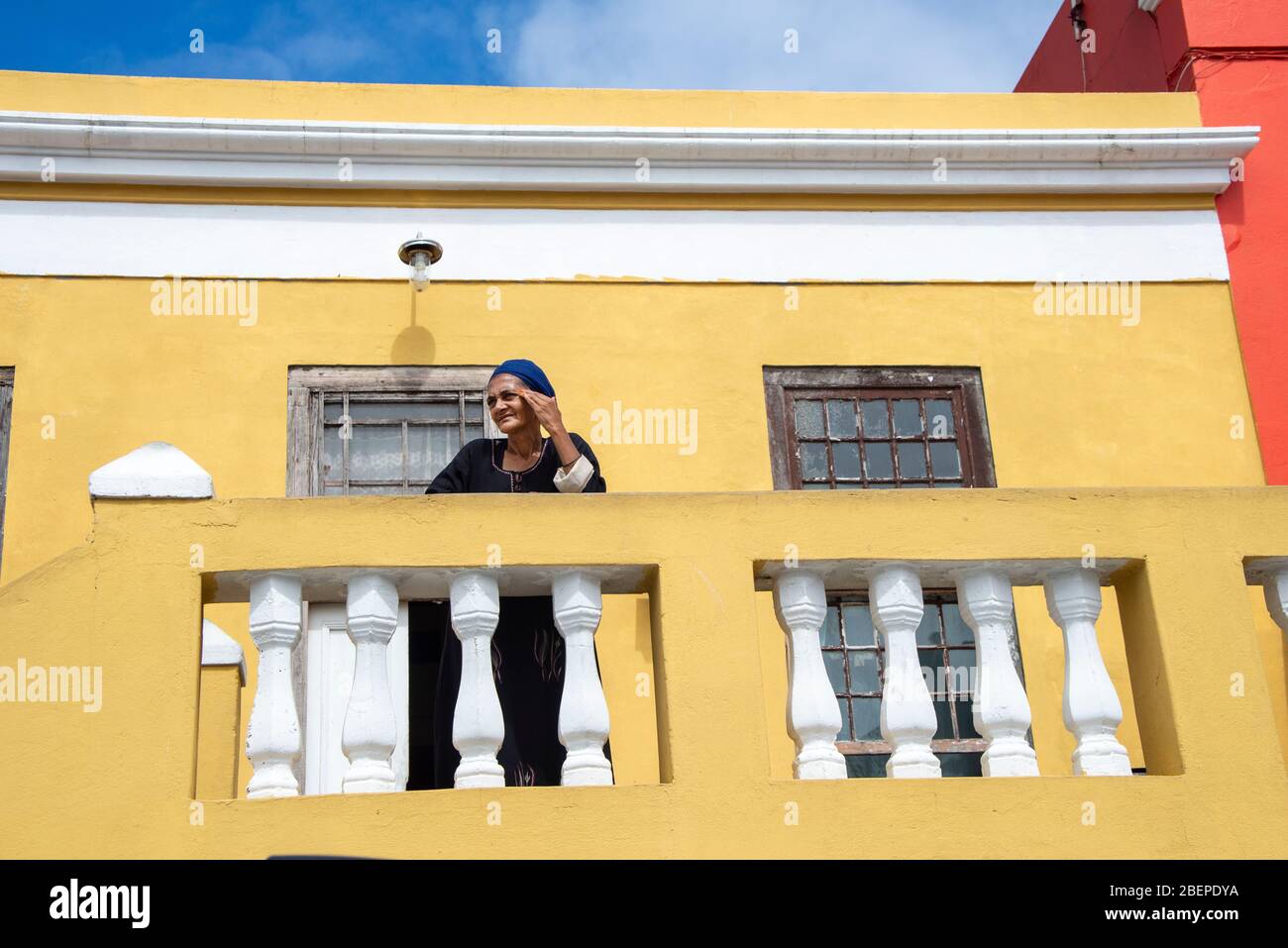 Eine muslimische Frau schaut von ihrem Haus im Bo-Kaap Bezirk in Kapstadt aus. Sie ist Teil der 'farbigen' Cape Malay Gemeinschaft, die dort lebt und die traditionellen Goldzähne hat. Bo-Kaap ist bekannt für seine farbenfrohen Häuser und gepflasterten Straßen. Die Gegend ist traditionell ein multikulturelles Viertel, und 56.9% der Bevölkerung identifizieren sich als Muslime. Nach Angaben der South African Heritage Resources Agency enthält das Gebiet die größte Konzentration von Architektur aus der Zeit vor 1850 in Südafrika und ist das älteste noch erhaltene Wohnviertel in Kapstadt. Stockfoto