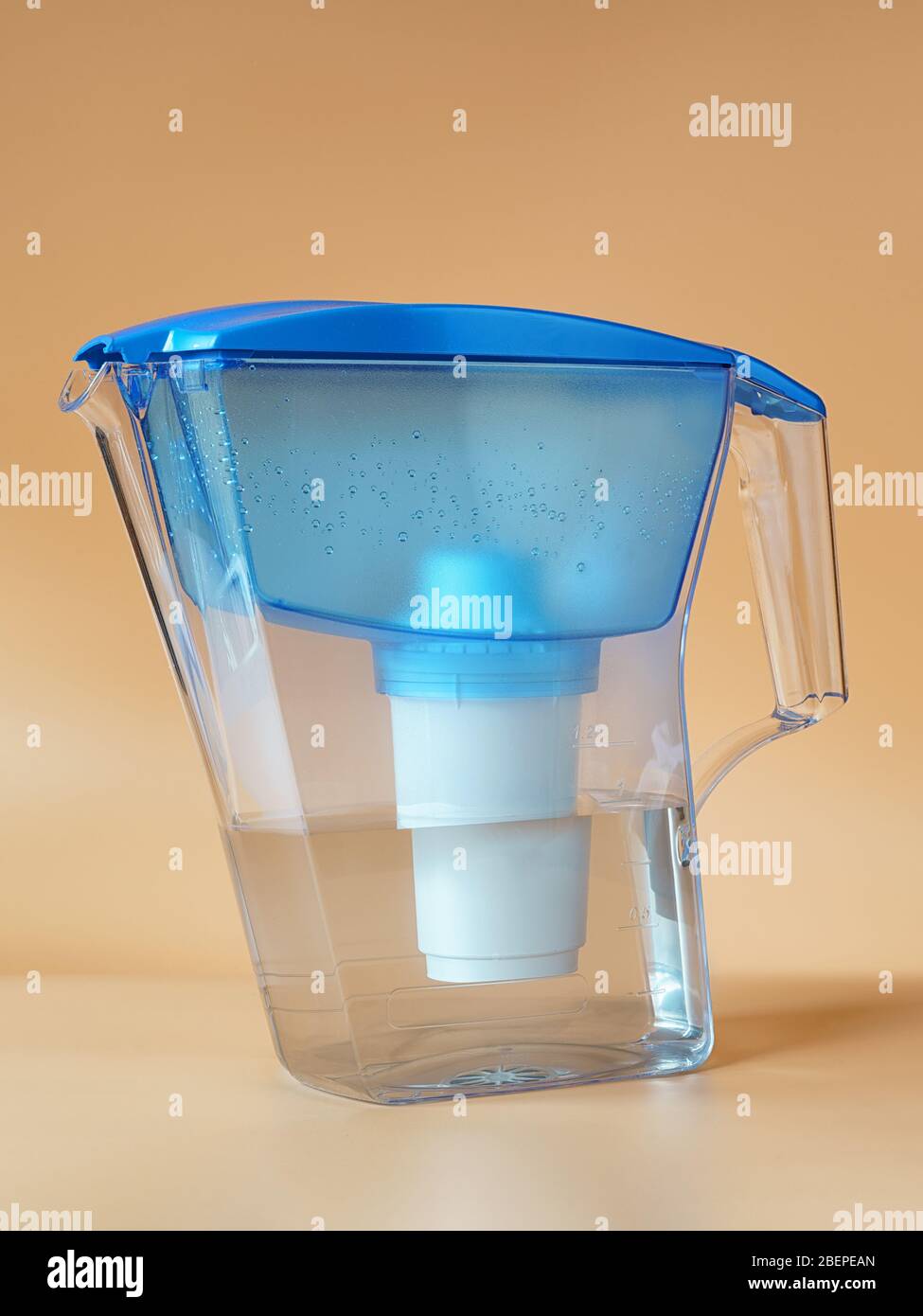 Durchsichtige Kunststoffkanne mit einem Wasserreiniger, der mit sauberem Wasser gefüllt ist. Auf beigefarbenem Hintergrund Stockfoto