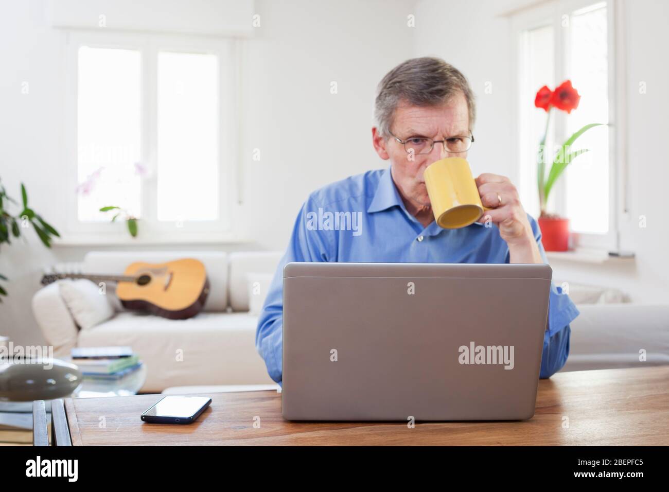 Ältere oder ältere Geschäftsmann trinken Kaffee vor einem Computer in seinem Home Office - konzentrieren Sie sich auf die Kante des Laptops Stockfoto