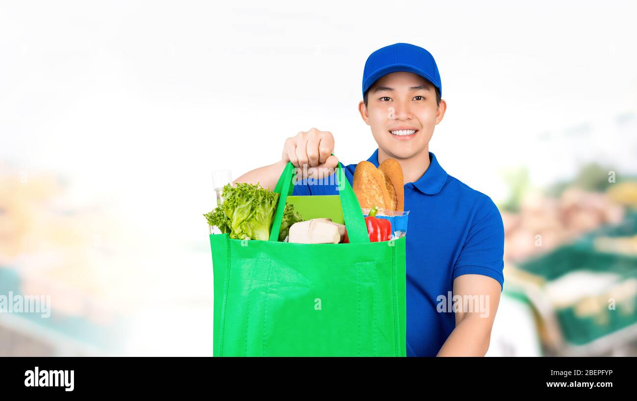 Lächelnder asiatischer Mann, der Lebensmitteleinkaufstasche im Supermarkt hält und Hauslieferdienst anbietet Stockfoto