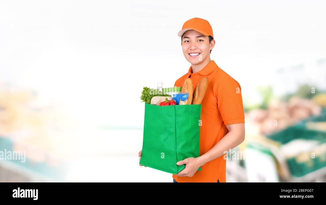 Hygienisch lächelnd asiatische Lieferung Mann mit Lebensmitteleinkaufstasche im Supermarkt Hintergrund Stockfoto